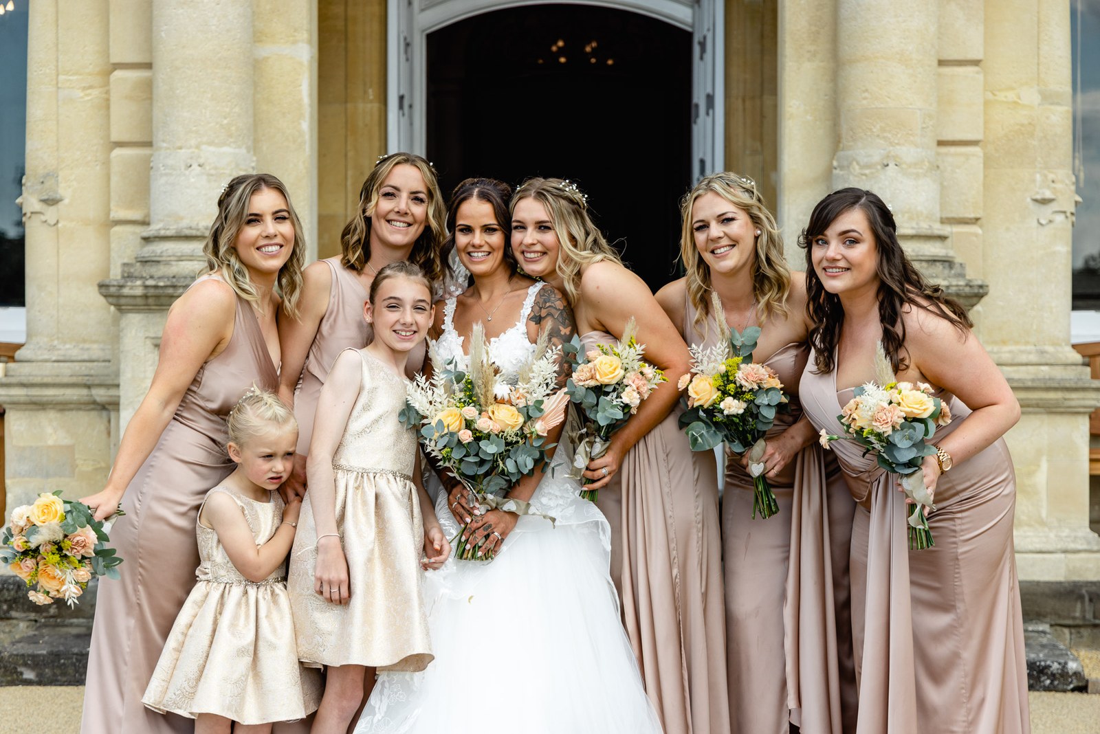 The bride with her bridesmaids and flower girls before a stone archway