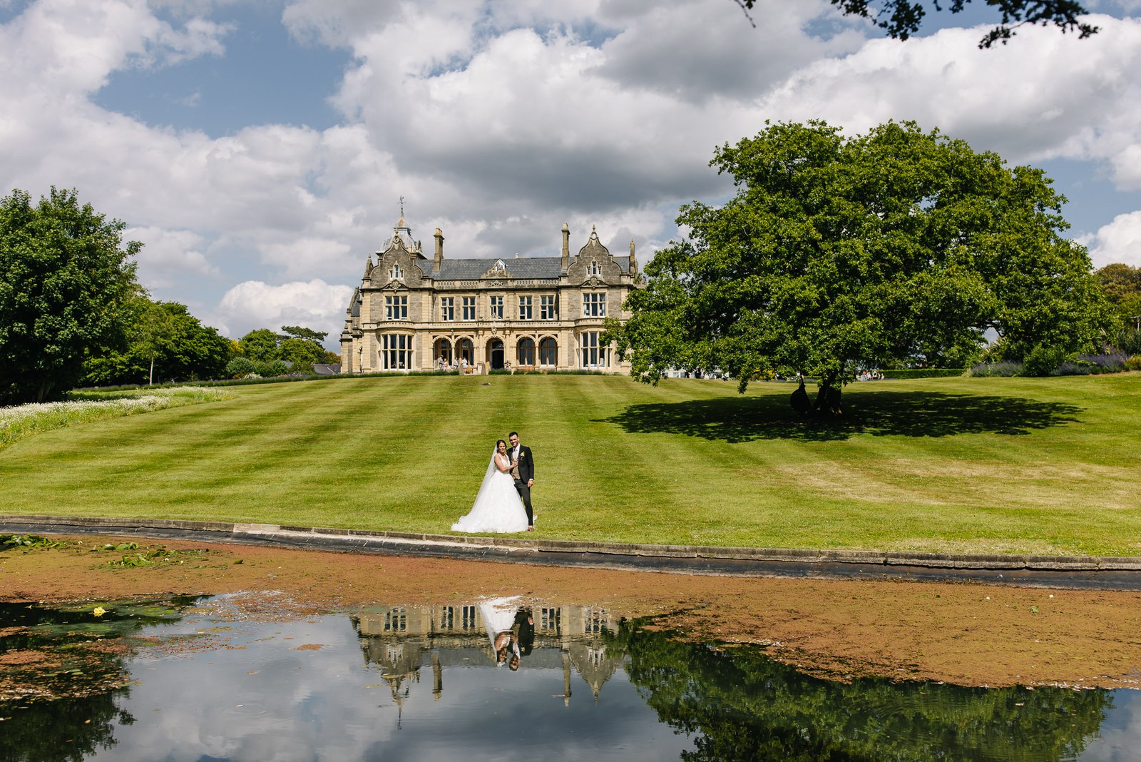 Clevedon Hall mirrored in the lake, the couple small on the sweeping lawn