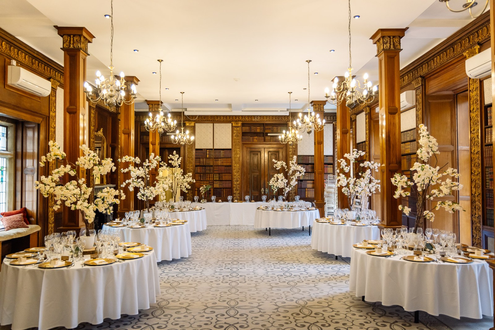The panelled library dressed with round tables and tall blossom centrepieces