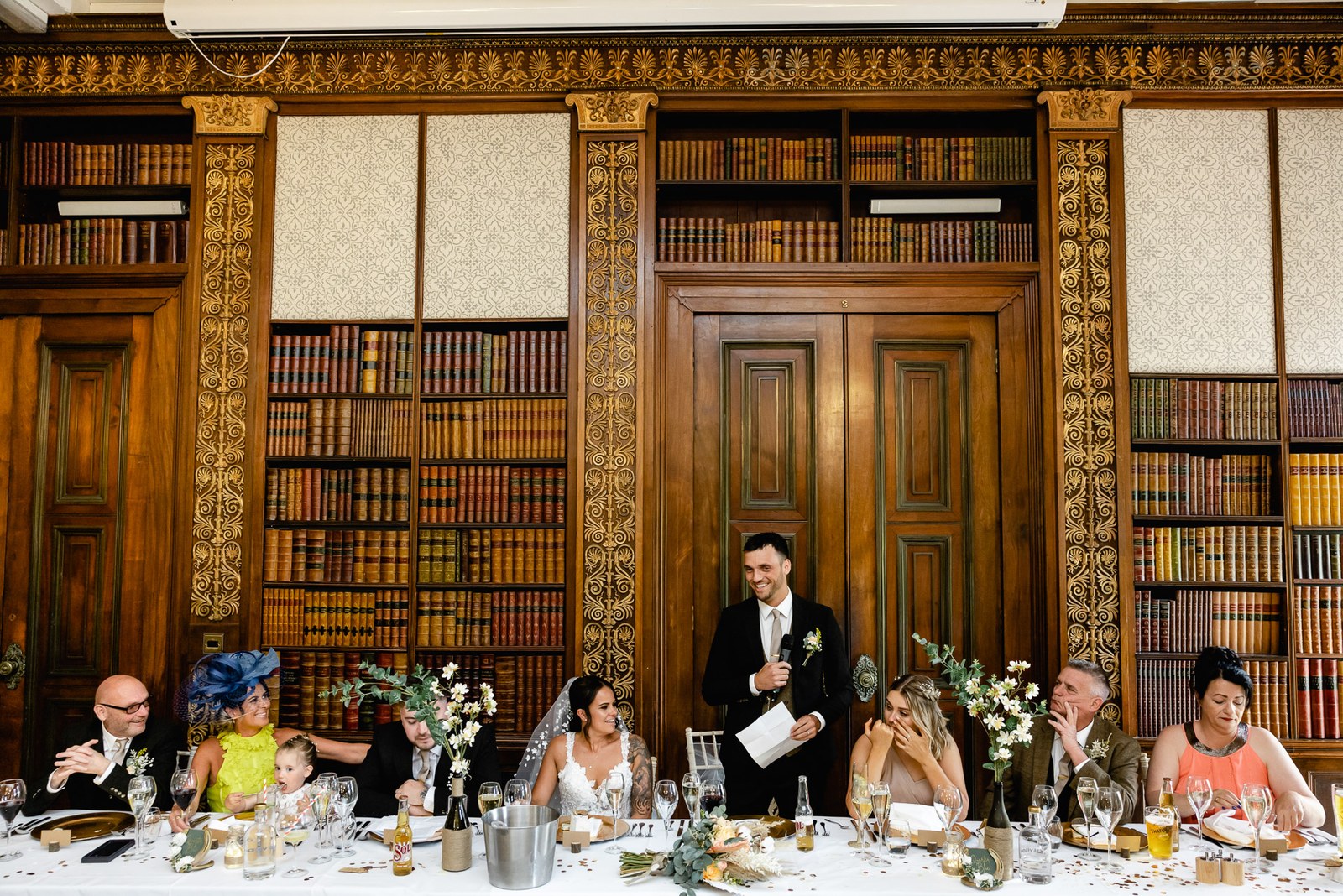 The groom gives his speech at the top table in Clevedon Hall's book-lined library