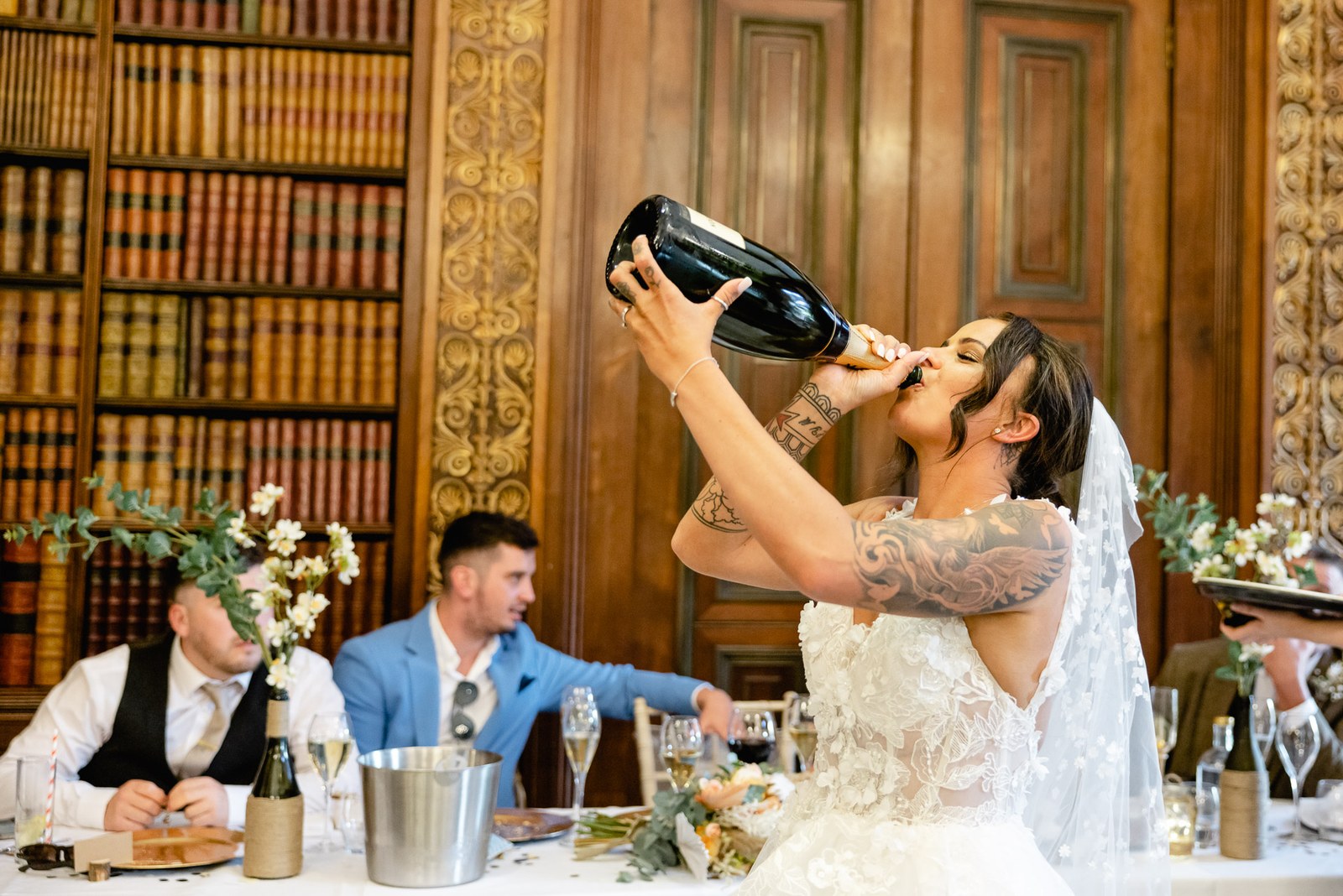 The bride tips a champagne bottle to drink from it at the top table