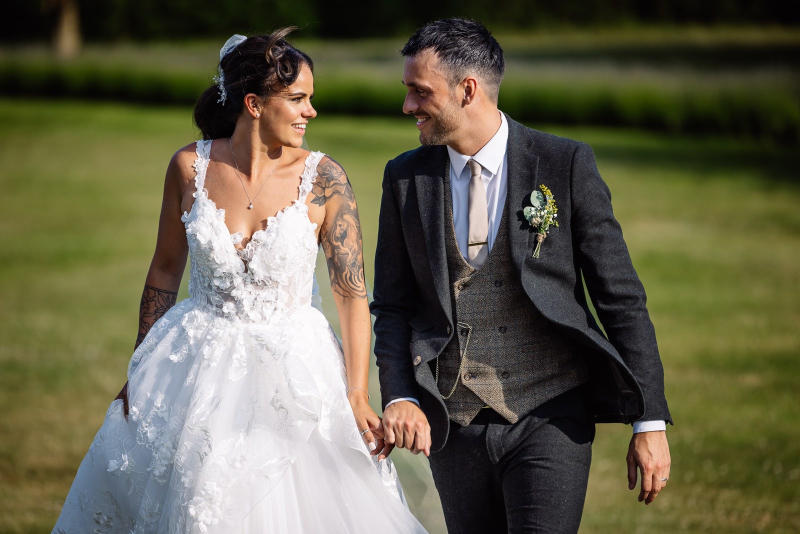 Bride and groom stroll hand in hand across the lawn, smiling at each other
