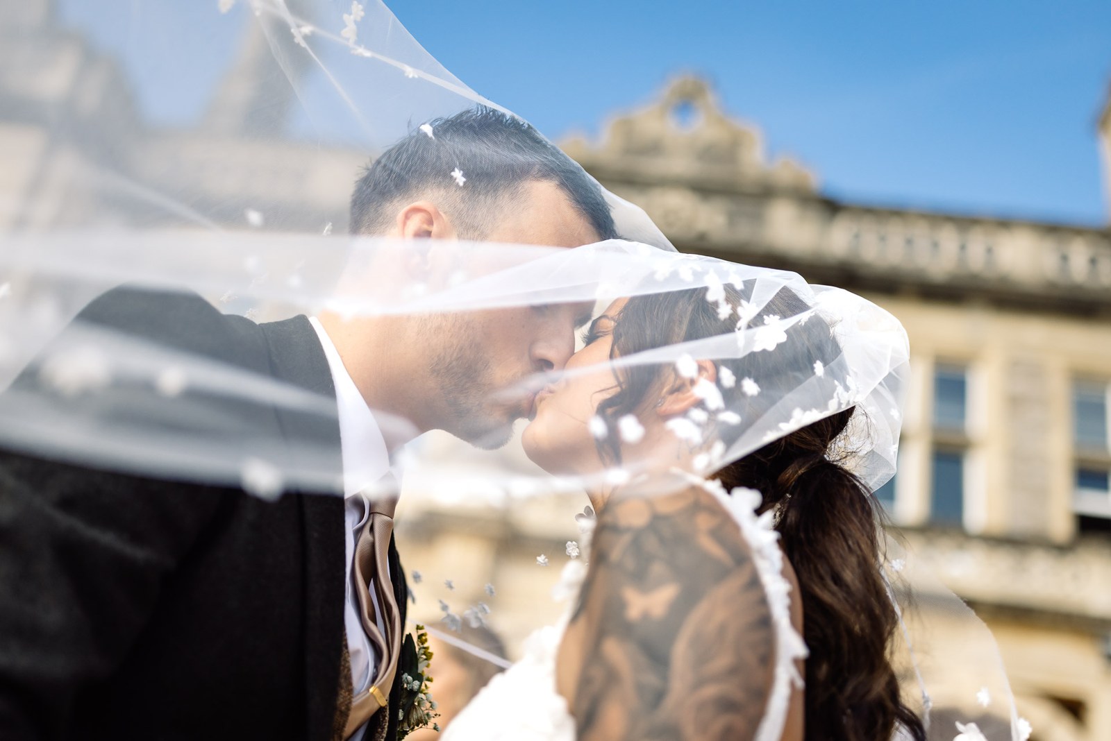 The couple kiss beneath the bride's veil against the venue's stone facade