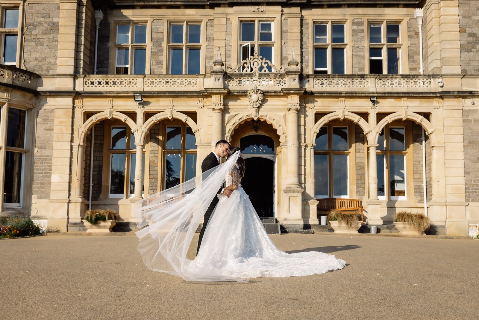 The couple before the Gothic stone facade of Clevedon Hall, the veil train spread wide