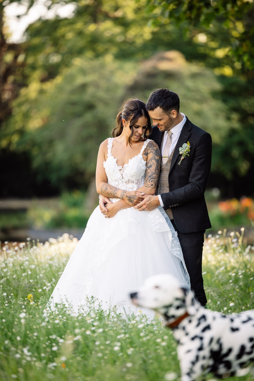The couple embrace in a wildflower meadow with the Dalmatian resting in the foreground