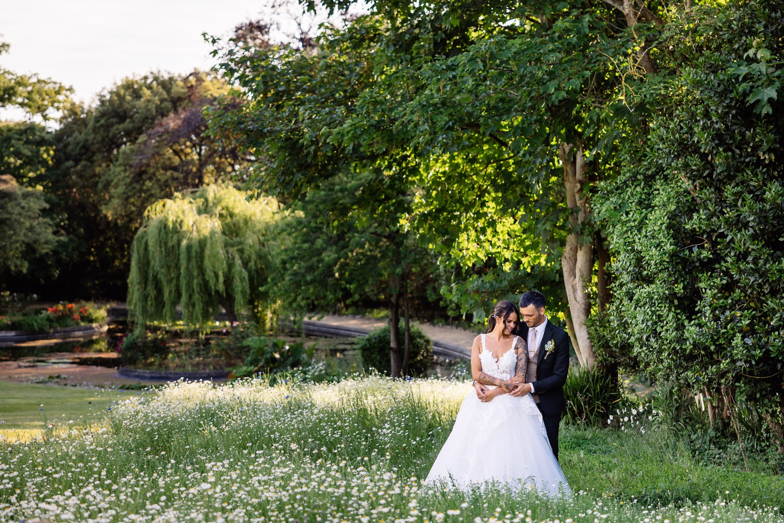 The couple stand small amid a wildflower meadow beside a willow and pond