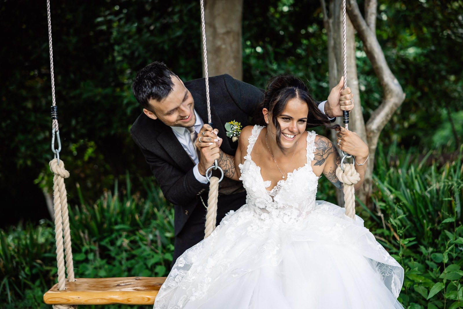 The groom and bride play on a rope tree swing in the garden