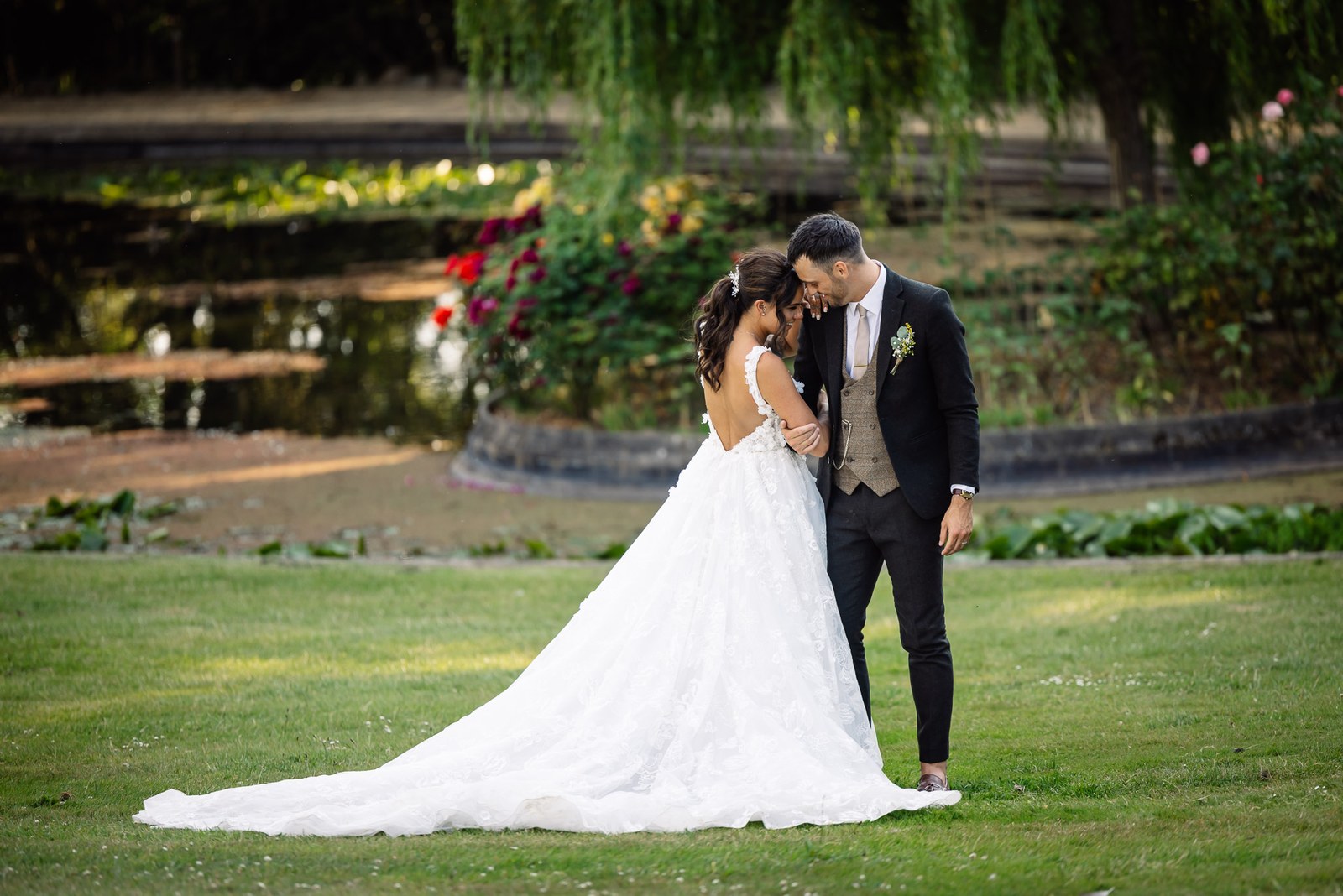 The couple rest forehead to forehead beside the garden pond