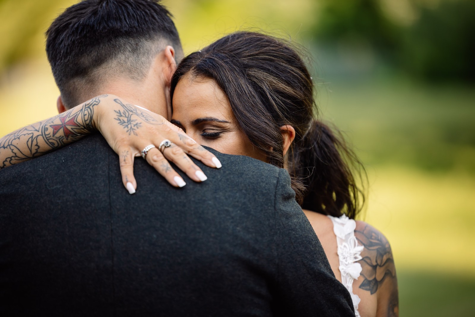 Close-up of the bride's ringed hand on the groom's shoulder as they embrace