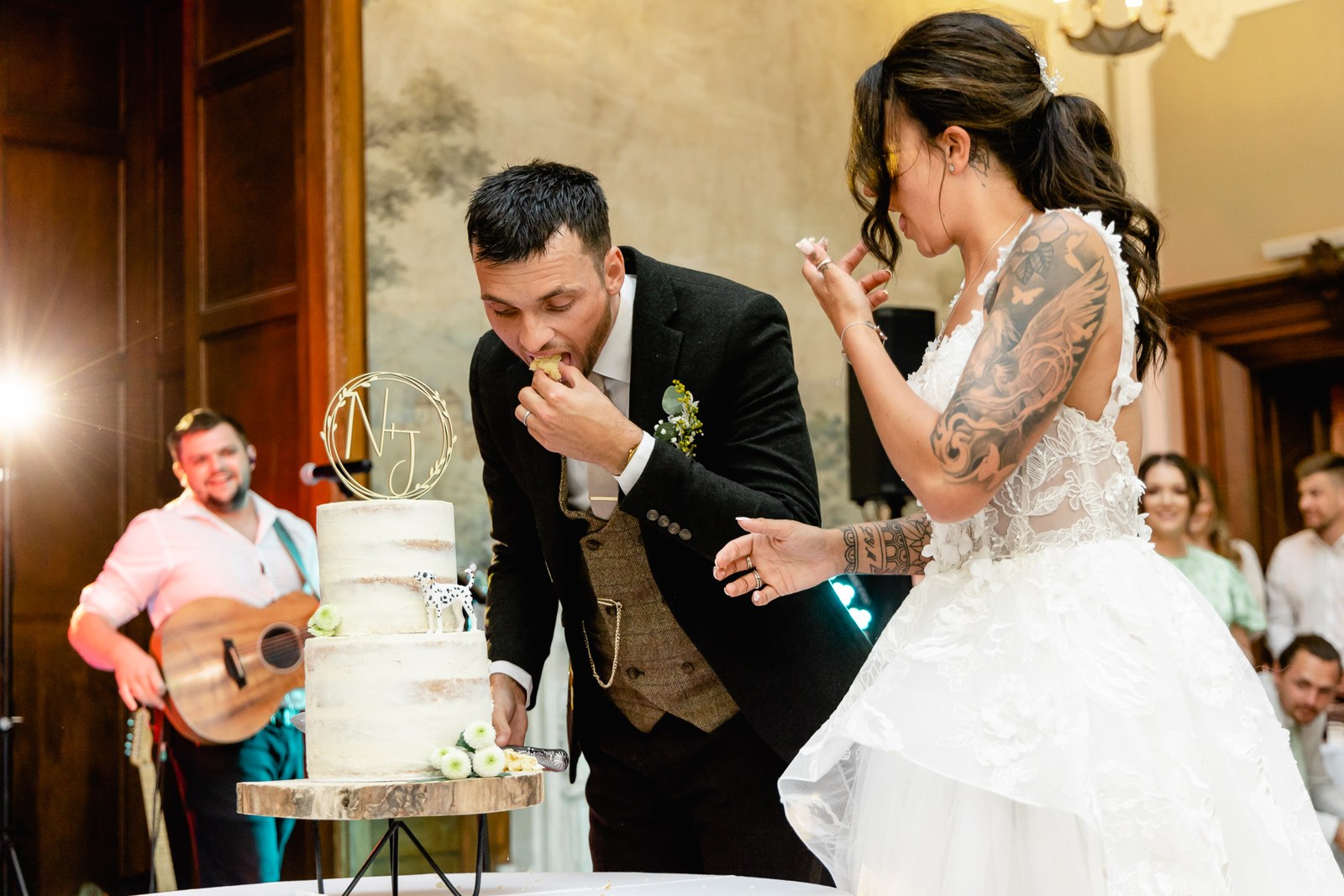 The groom tastes cake as the couple cut it beside a guitarist