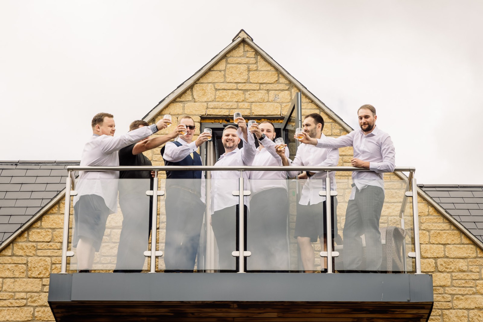 Groomsmen in shirtsleeves raise a toast on a balcony at Cotswolds Hotel & Spa