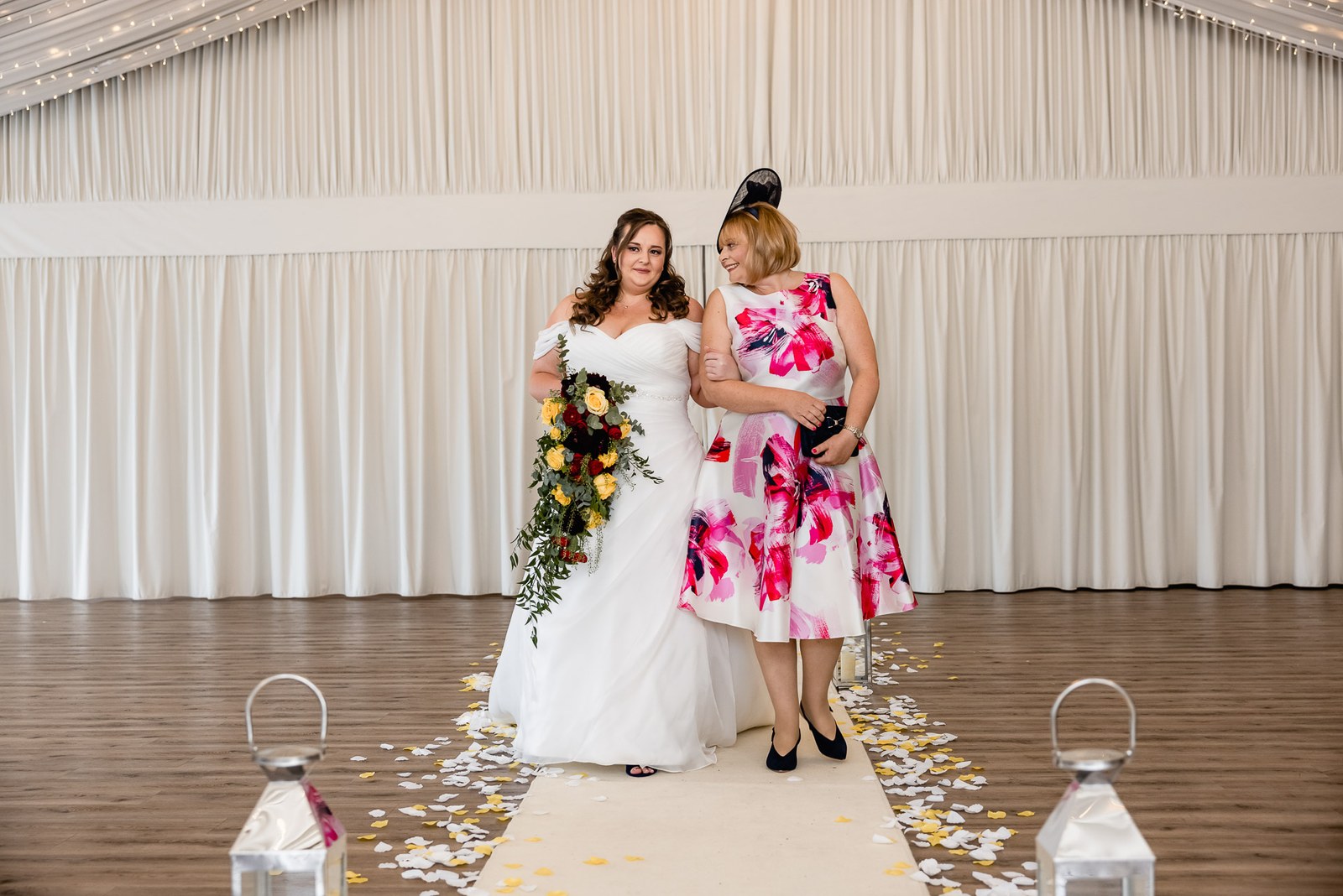 The bride and her mother pause on the petal aisle in the draped ceremony room