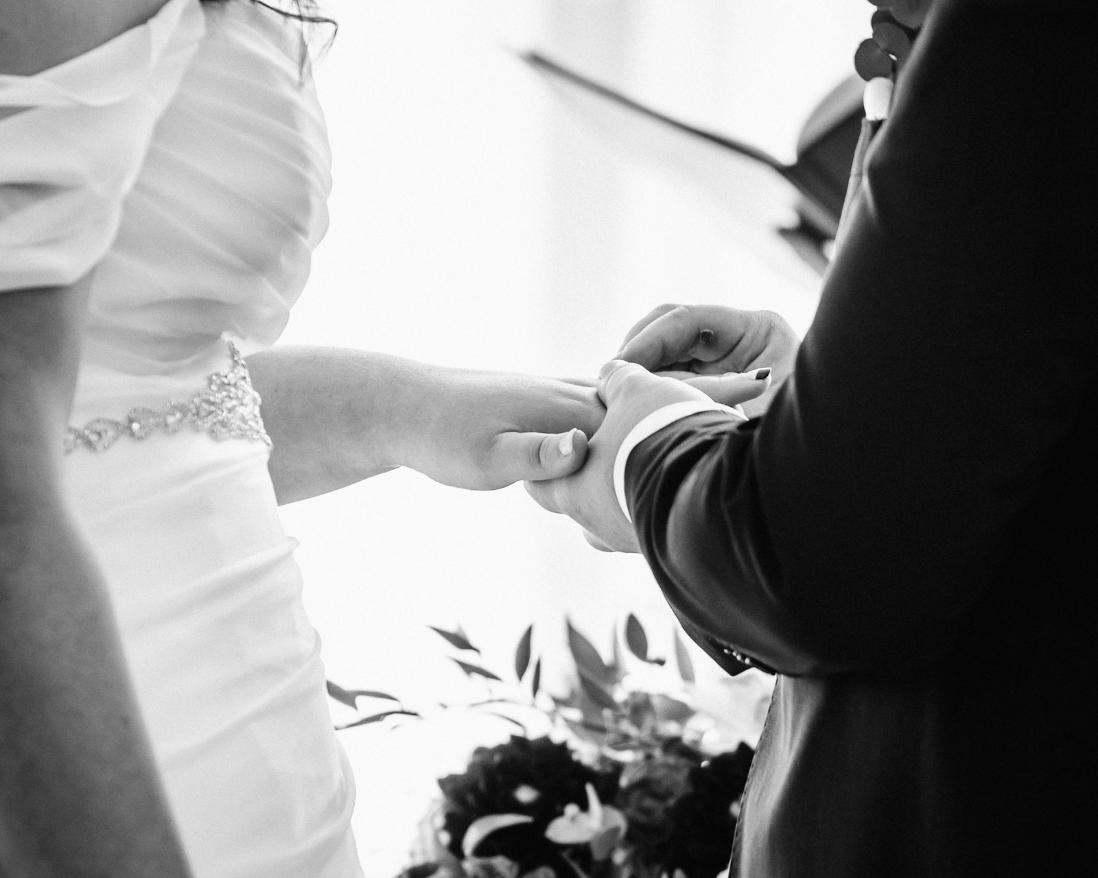 Black-and-white close-up of the ring being placed on the bride's finger
