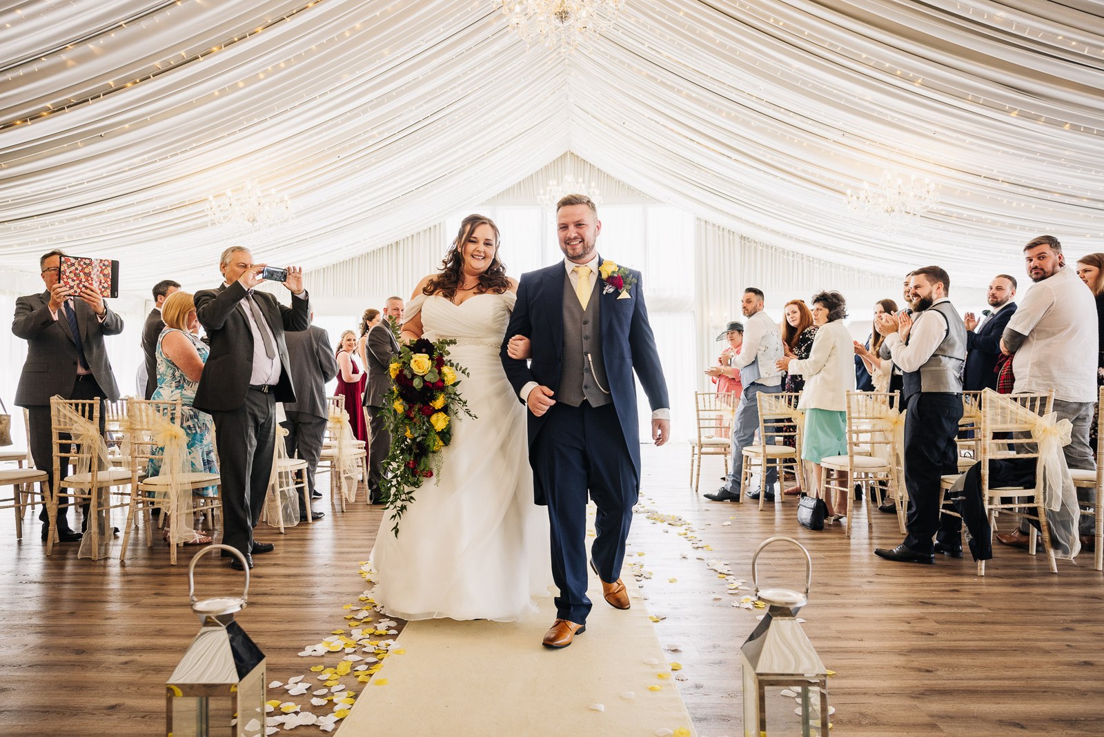 The newlyweds walk back down the aisle as guests applaud in the draped pavilion