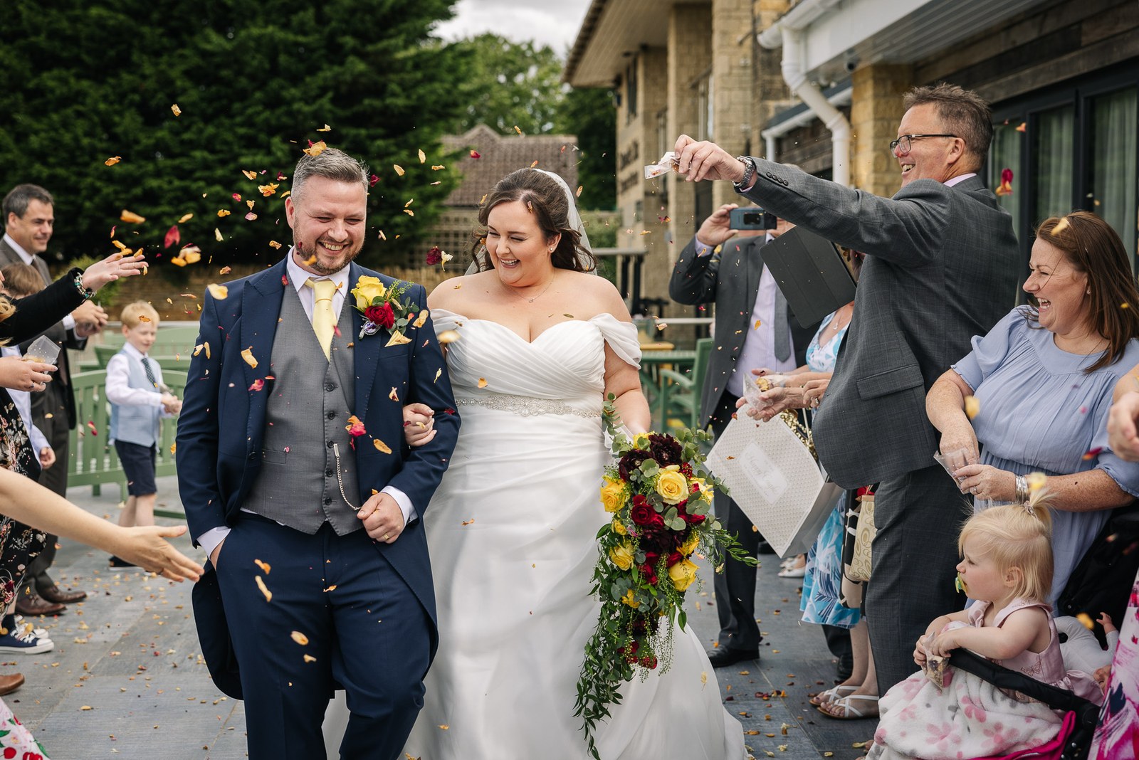 Confetti falls as the couple leave the stone hotel building at Cotswolds Hotel & Spa