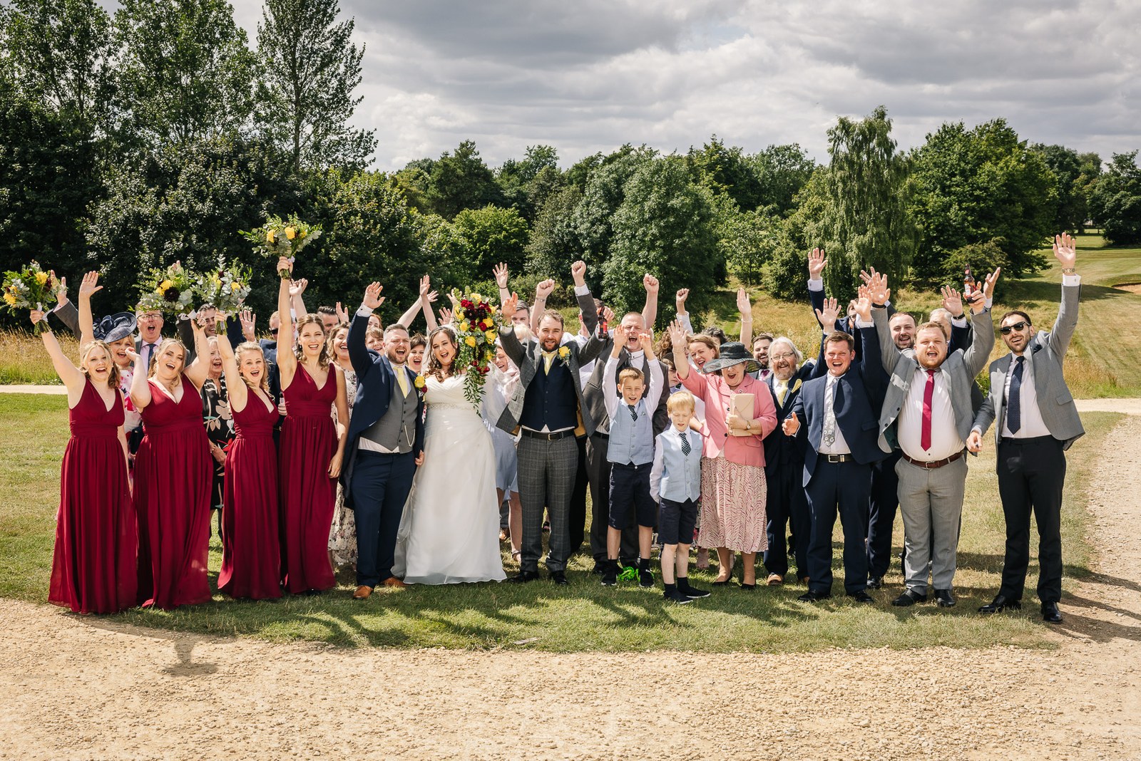 Wedding guests raise their arms for a group photo on the golf course lawns