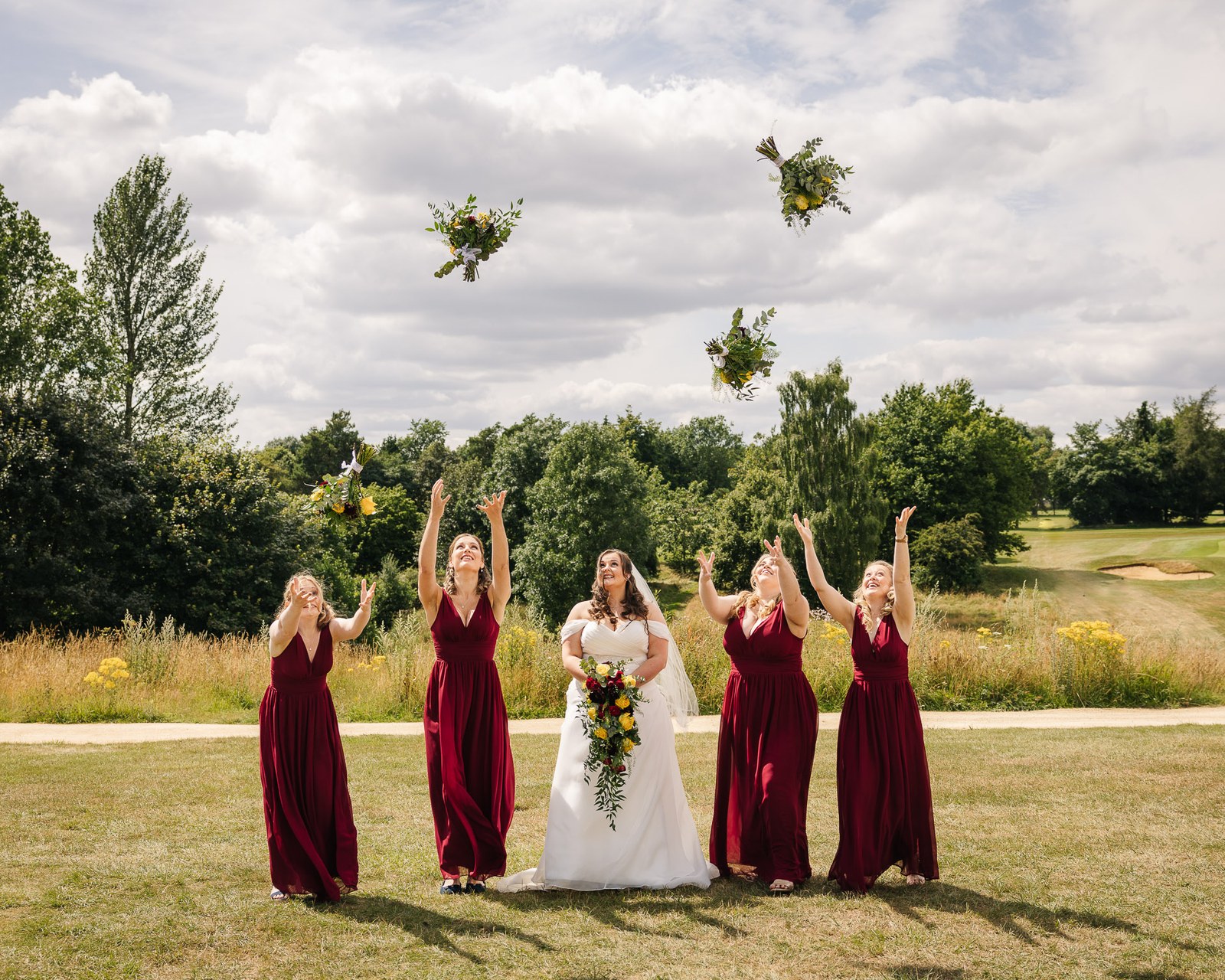 The bridesmaids toss their bouquets into the air beside the bride on the golf course