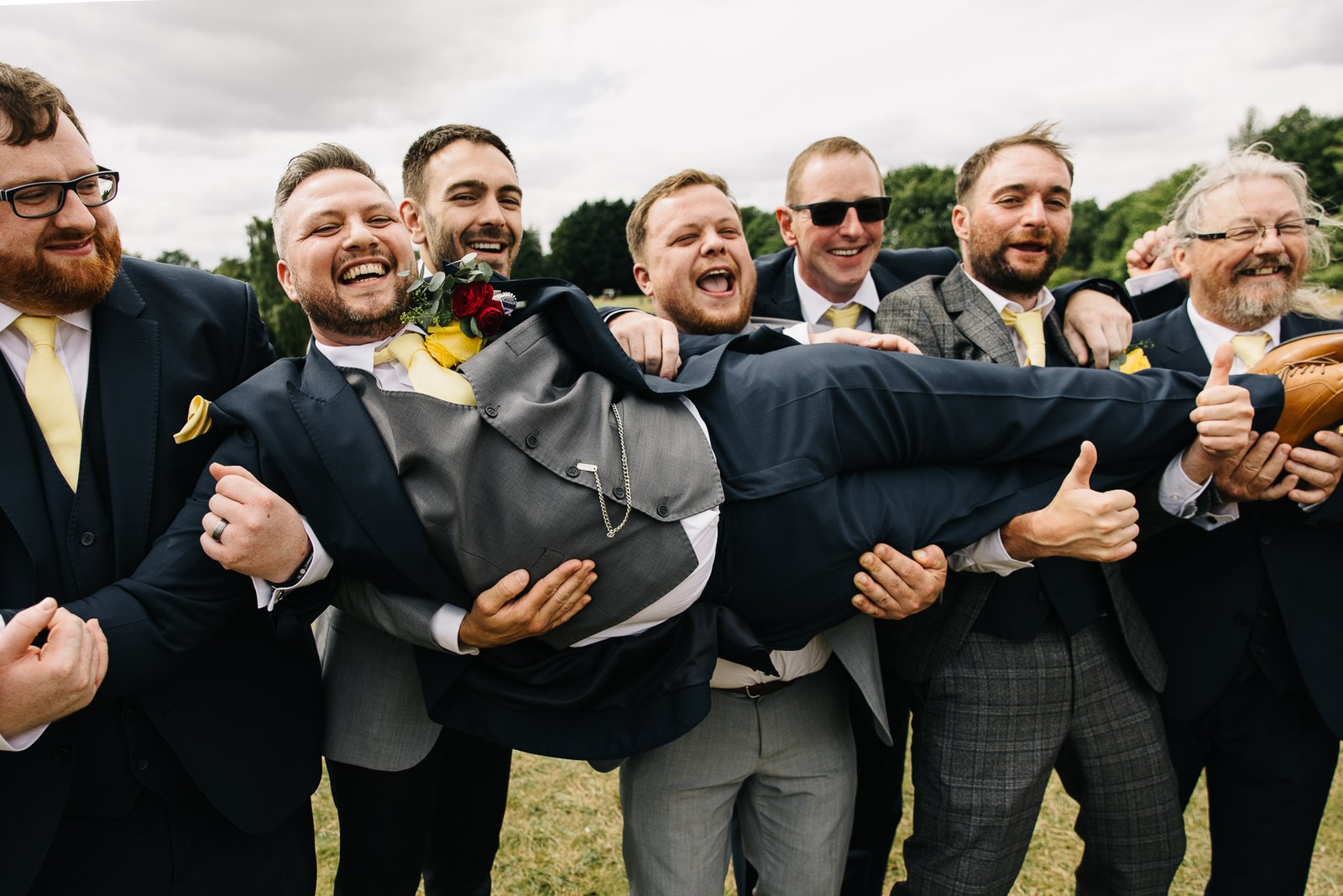 The groomsmen hoist the groom horizontally into the air, all laughing