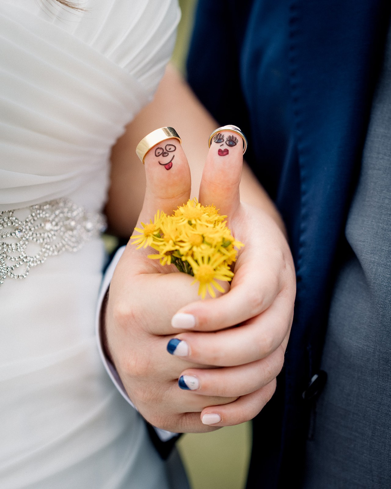 Close-up of the couple's clasped hands with faces drawn on their fingers holding daisies