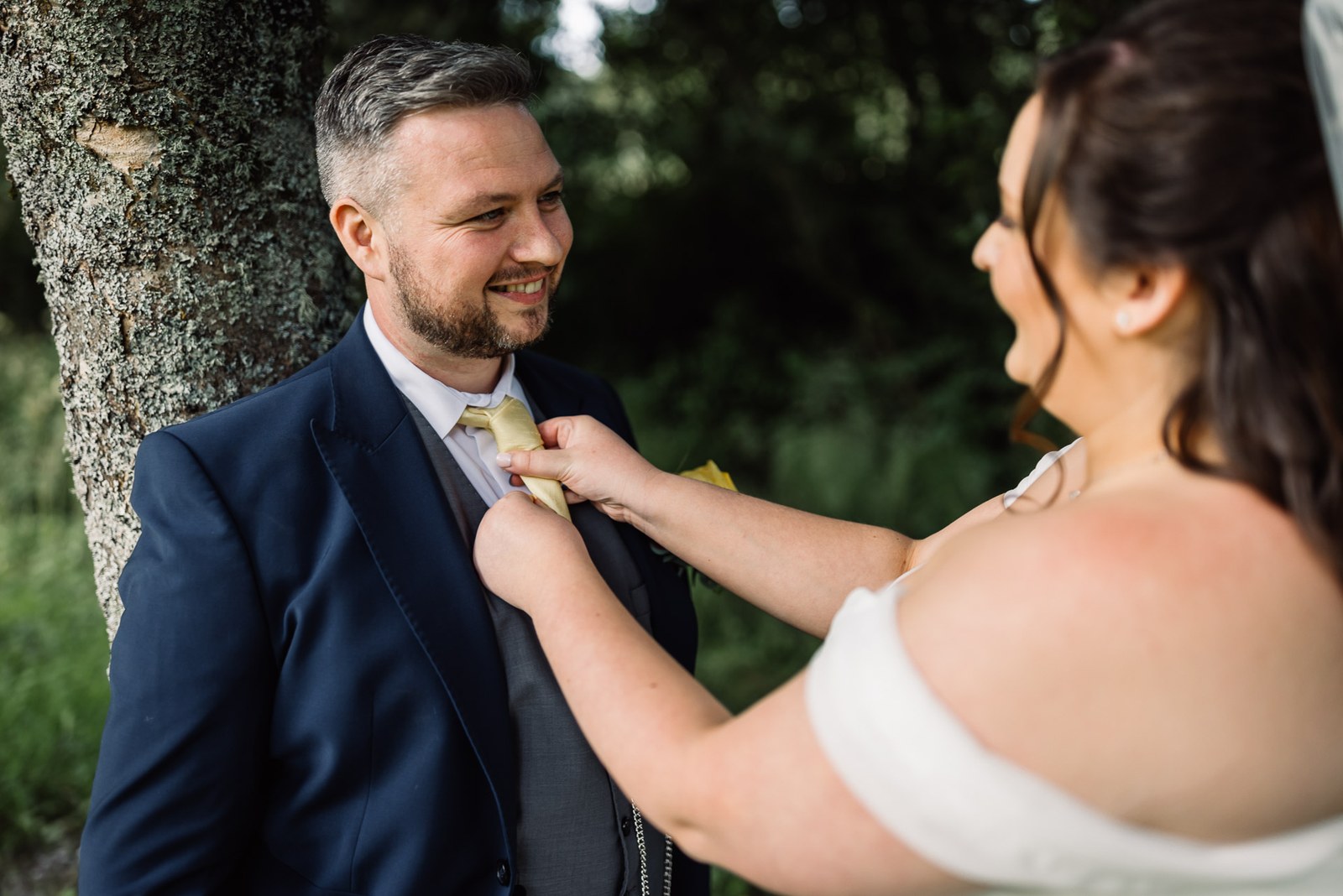 The bride adjusts the groom's tie beneath a tree