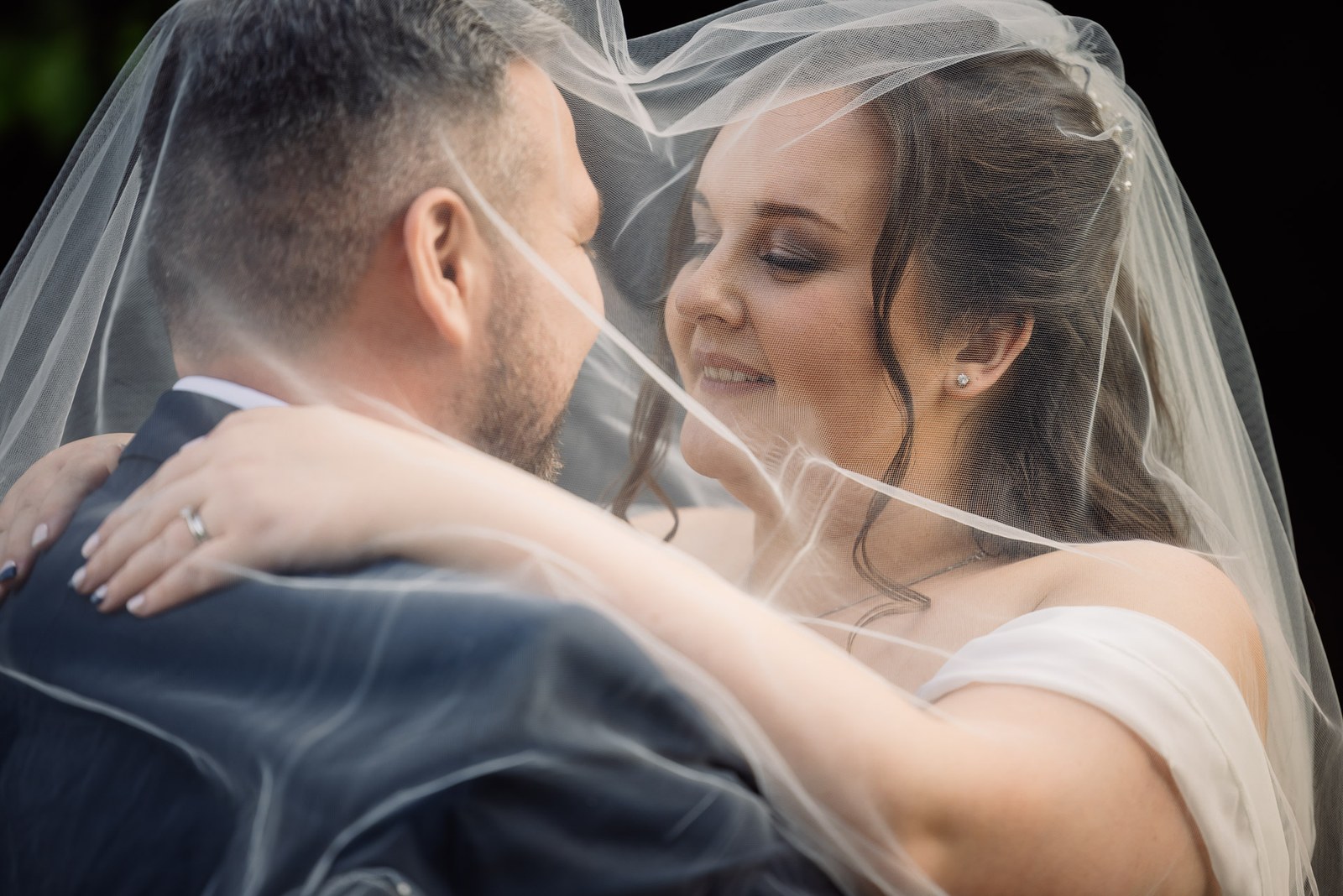The couple hold each other beneath the bride's veil, her ring on show