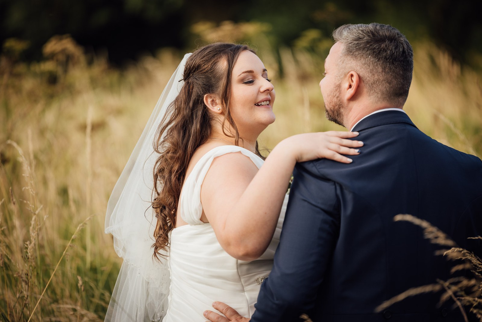 The couple stand face to face among the long grasses