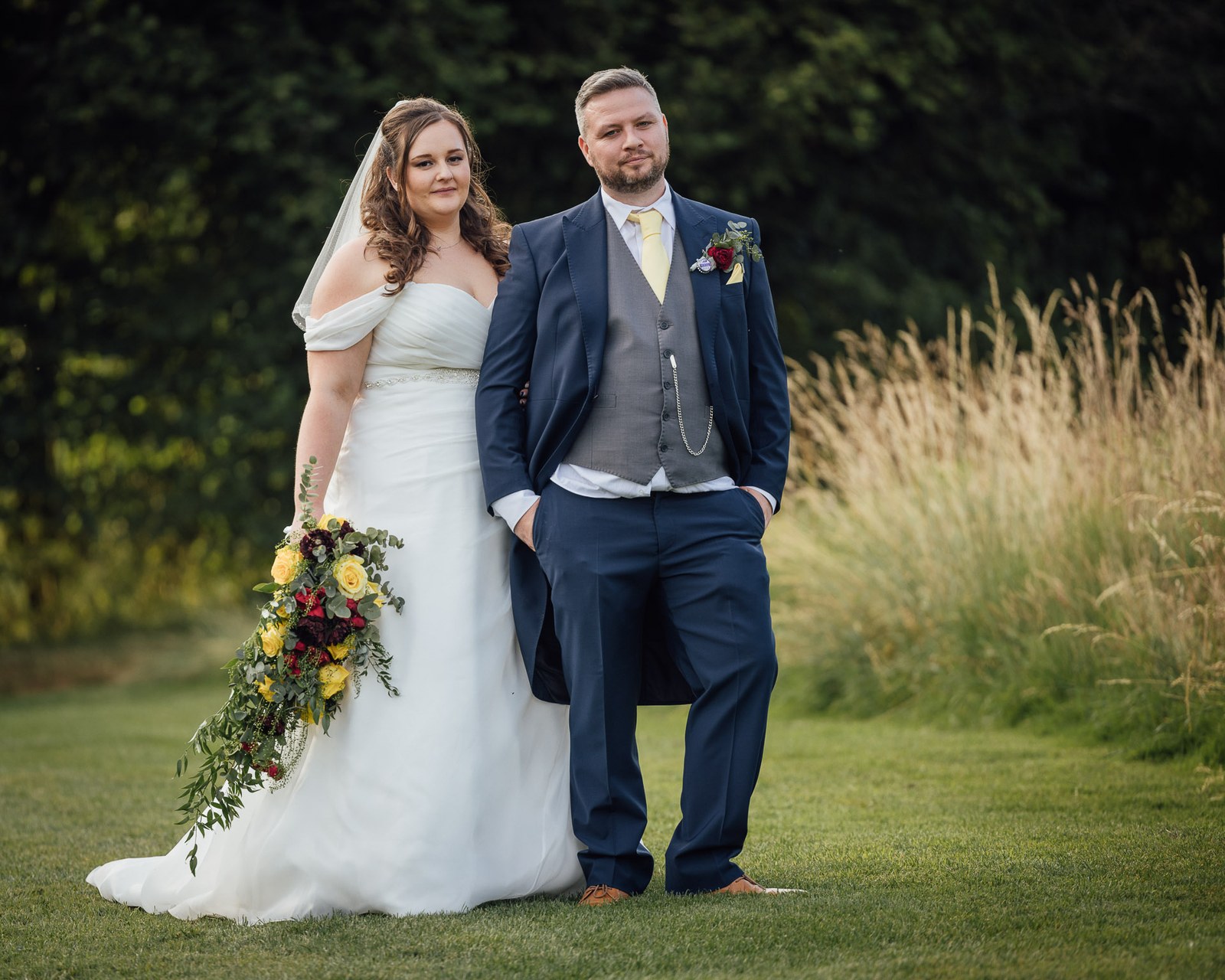 The couple in the long grass, the bride holding her cascading bouquet