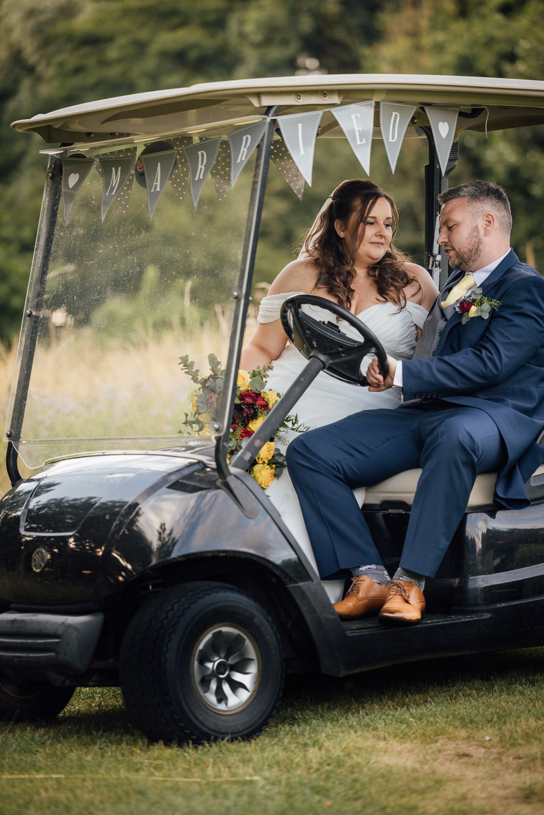 The couple sit together in a bunting-trimmed golf buggy at Cotswolds Hotel & Spa
