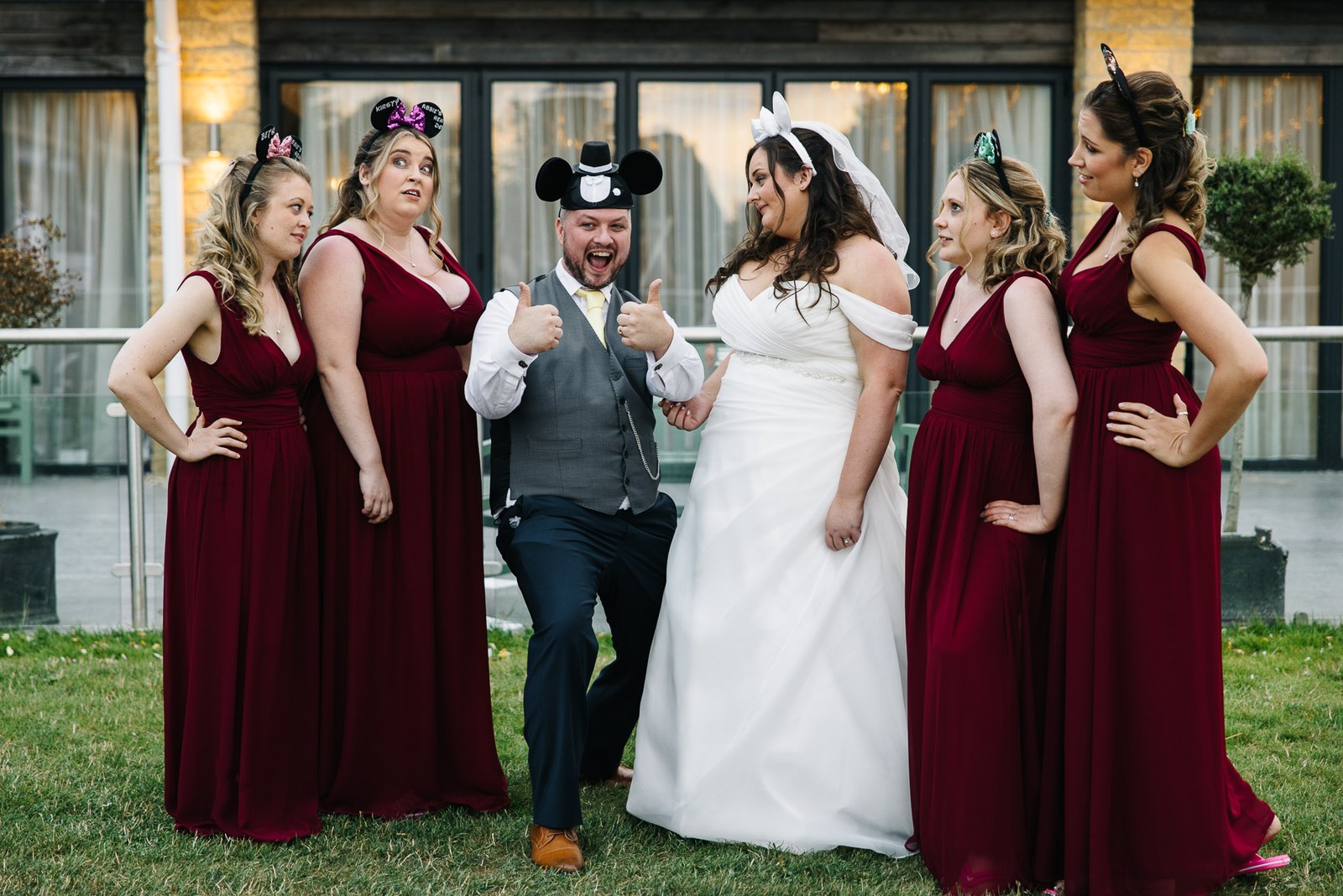 The groom in novelty mouse ears larks about with the bridesmaids on the lawn