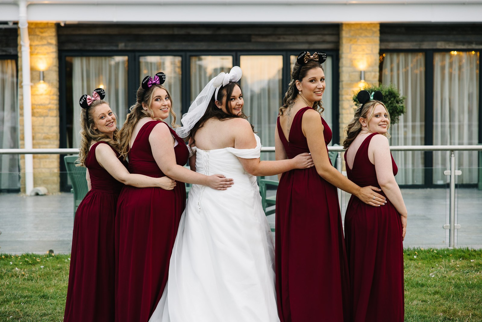 The bride embraces her bridesmaids in red outside the hotel
