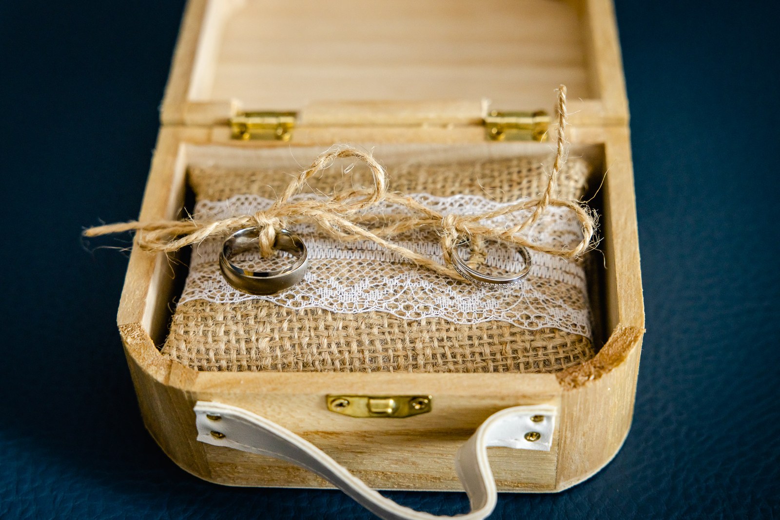 Two wedding rings resting on hessian and lace inside a small wooden ring box