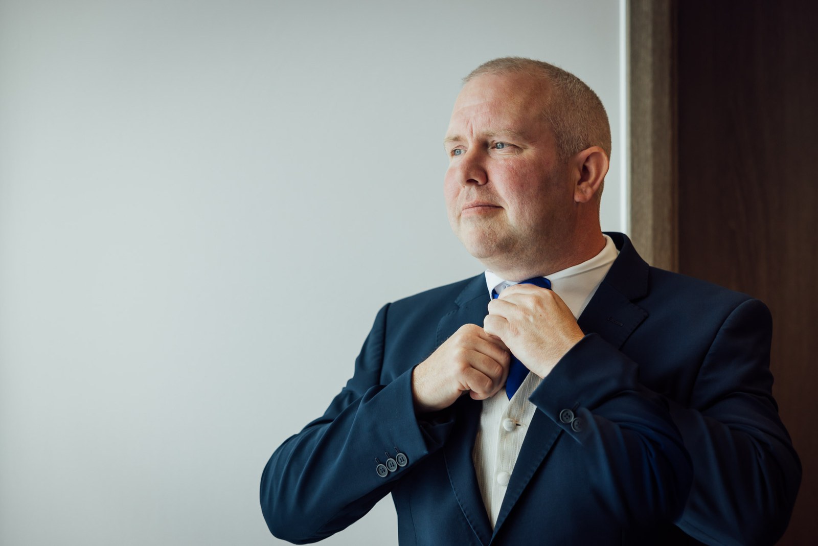 Groom in a navy suit straightening his blue tie before the ceremony