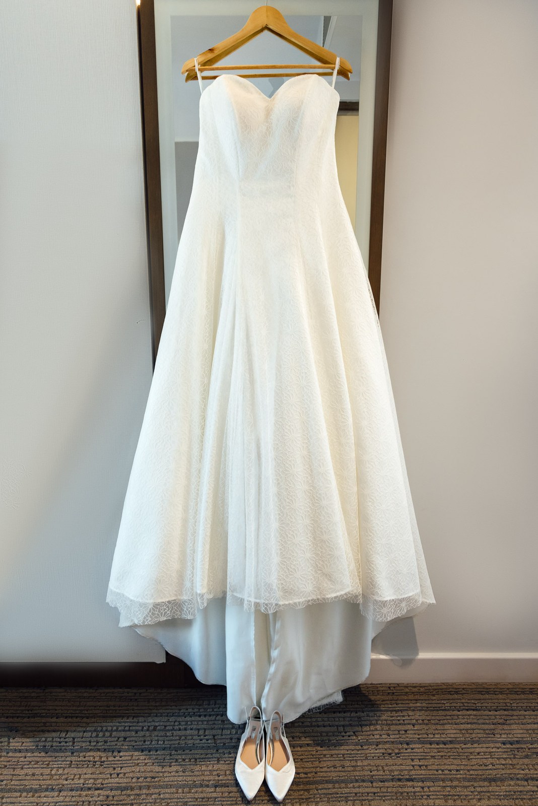 The bride's strapless white gown on a hanger with pointed heels waiting below