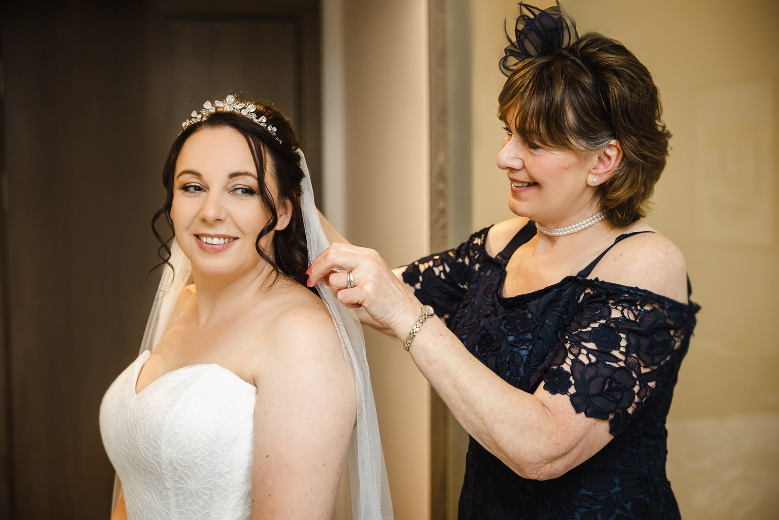 Mother of the bride fixing the veil as the bride smiles, wearing a sparkling tiara