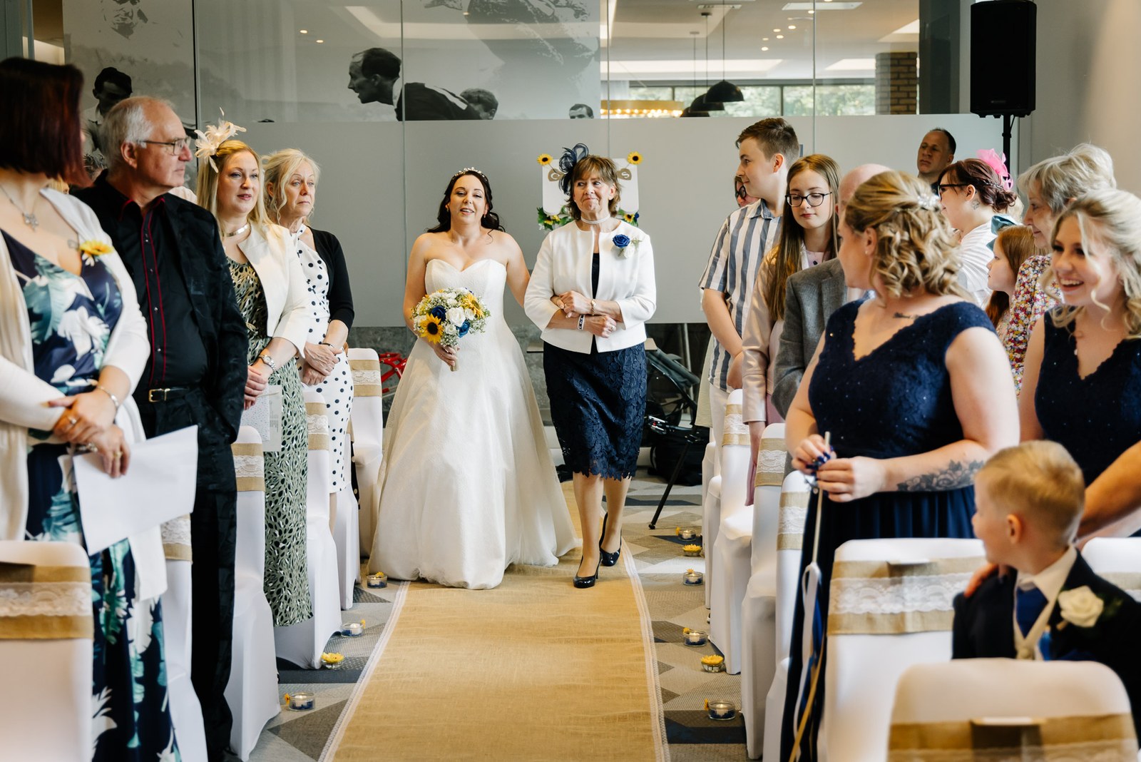 The bride walking down the aisle with a sunflower bouquet as guests look on