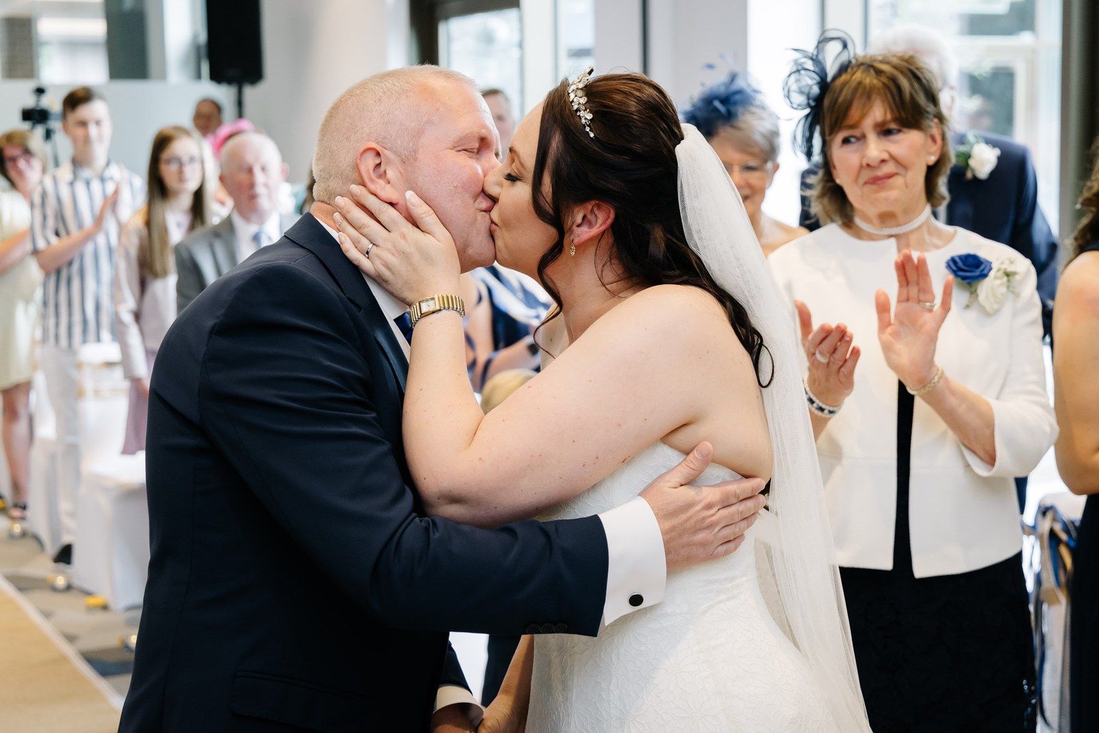 The newlyweds sharing their first kiss as married partners while guests applaud