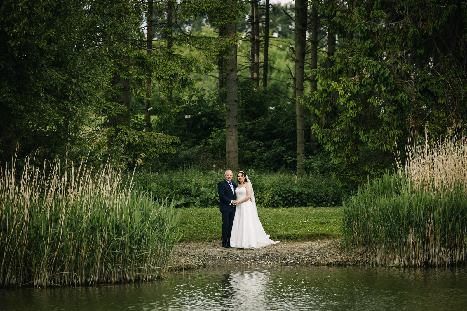 The couple beside a reed-fringed lake in summer greenery