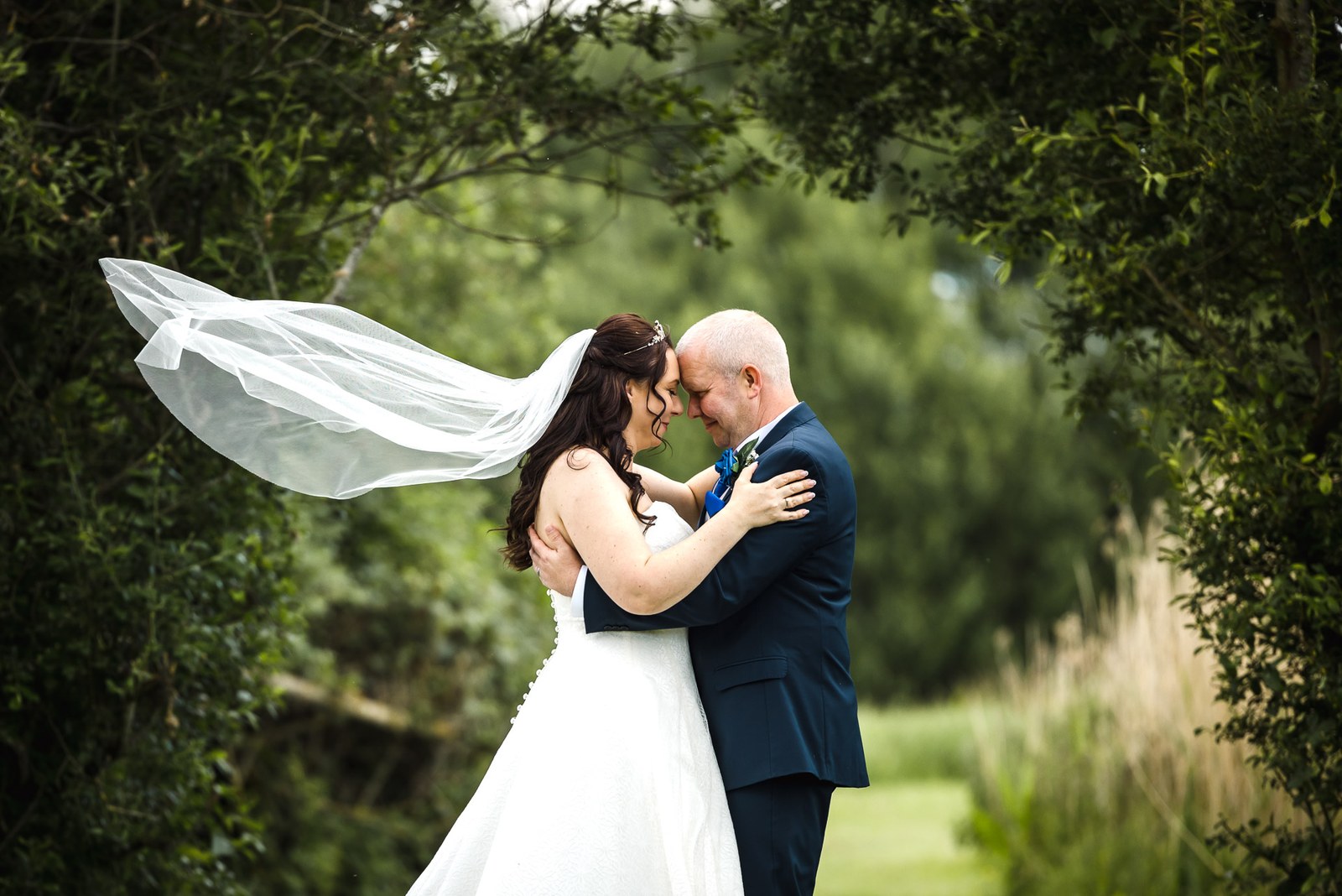 The couple nose to nose as the bride's veil lifts in the breeze