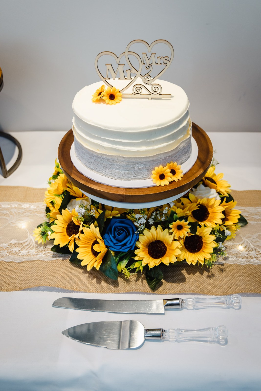 A single-tier cake trimmed with sunflowers and a blue rose beside the cutting knife