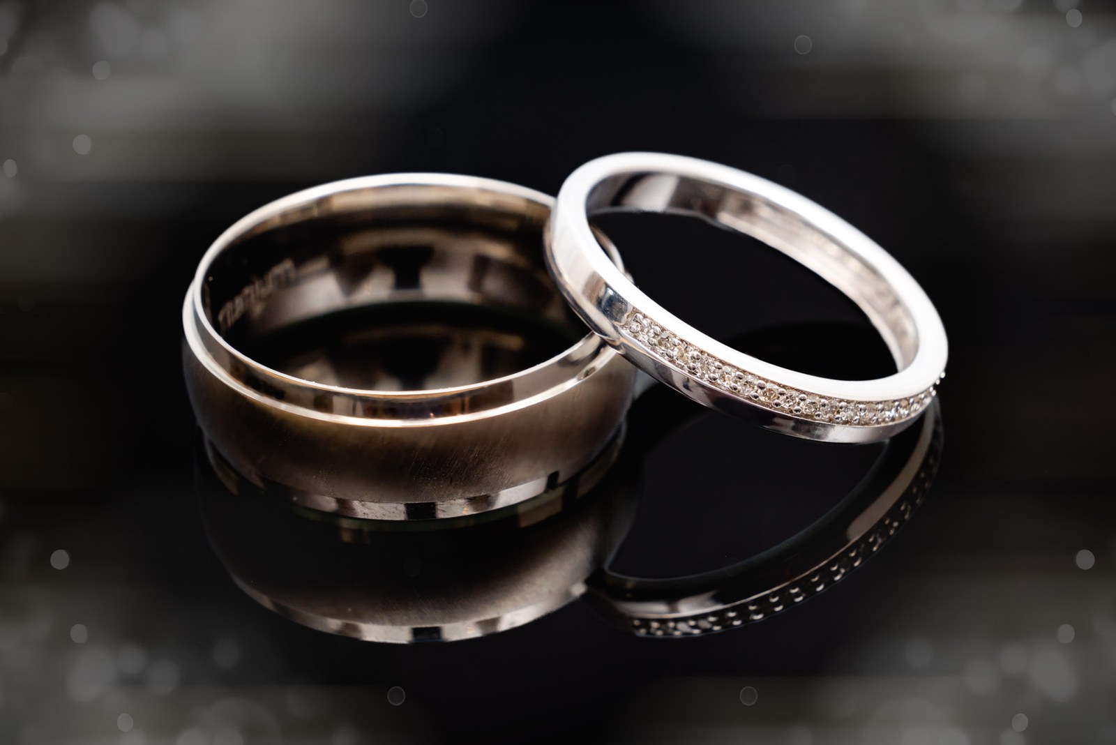Close-up of the wedding bands, one plain and one set with diamante, on a dark ground
