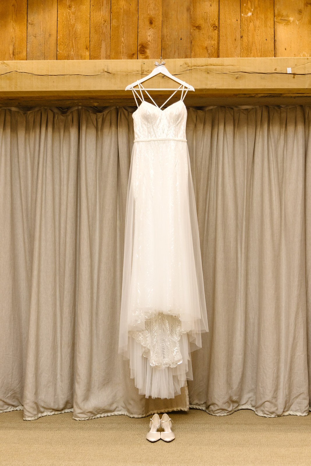 The bride's gown hanging against curtains in a panelled room, her shoes waiting below