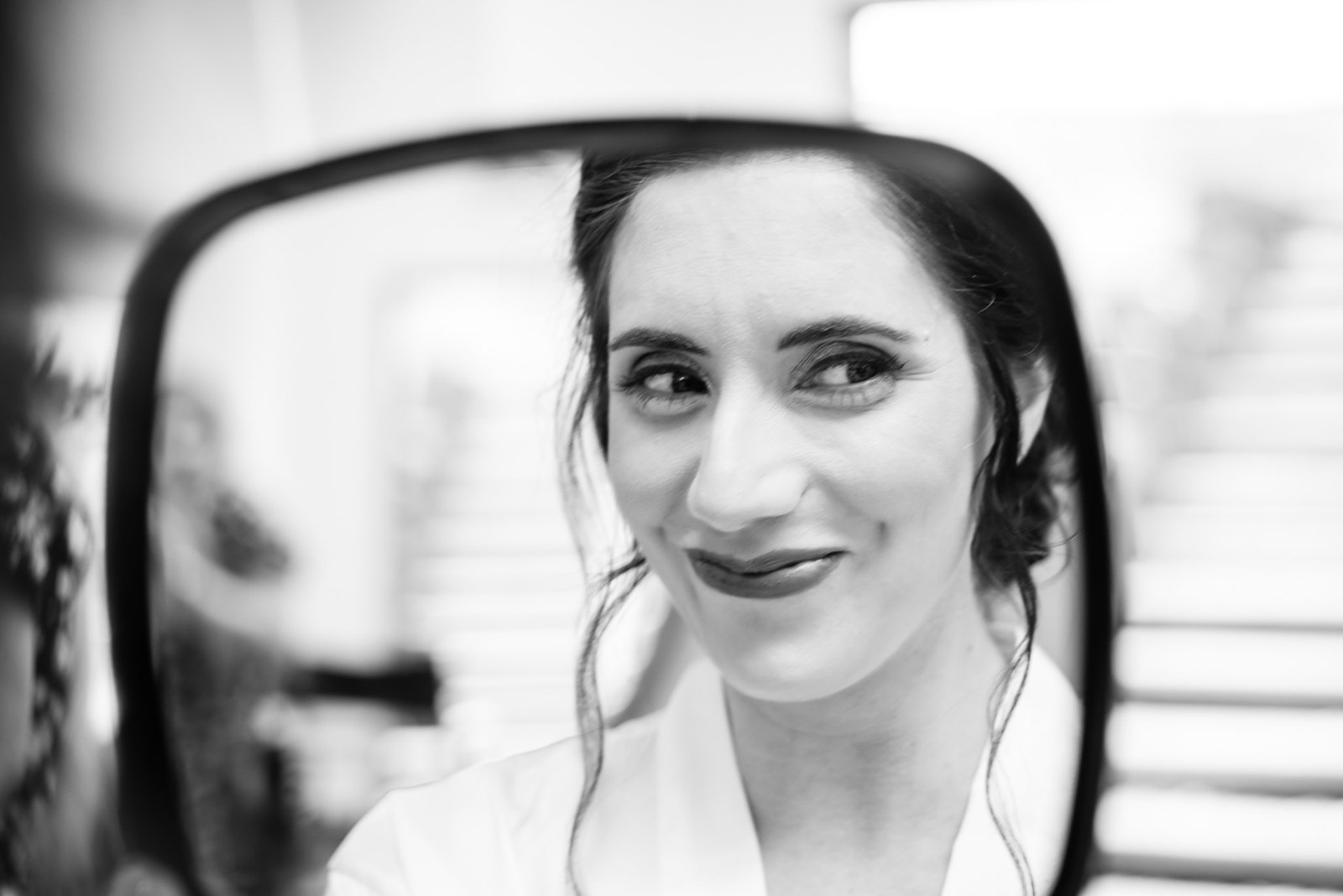 Black-and-white reflection of the bride smiling in a hand mirror