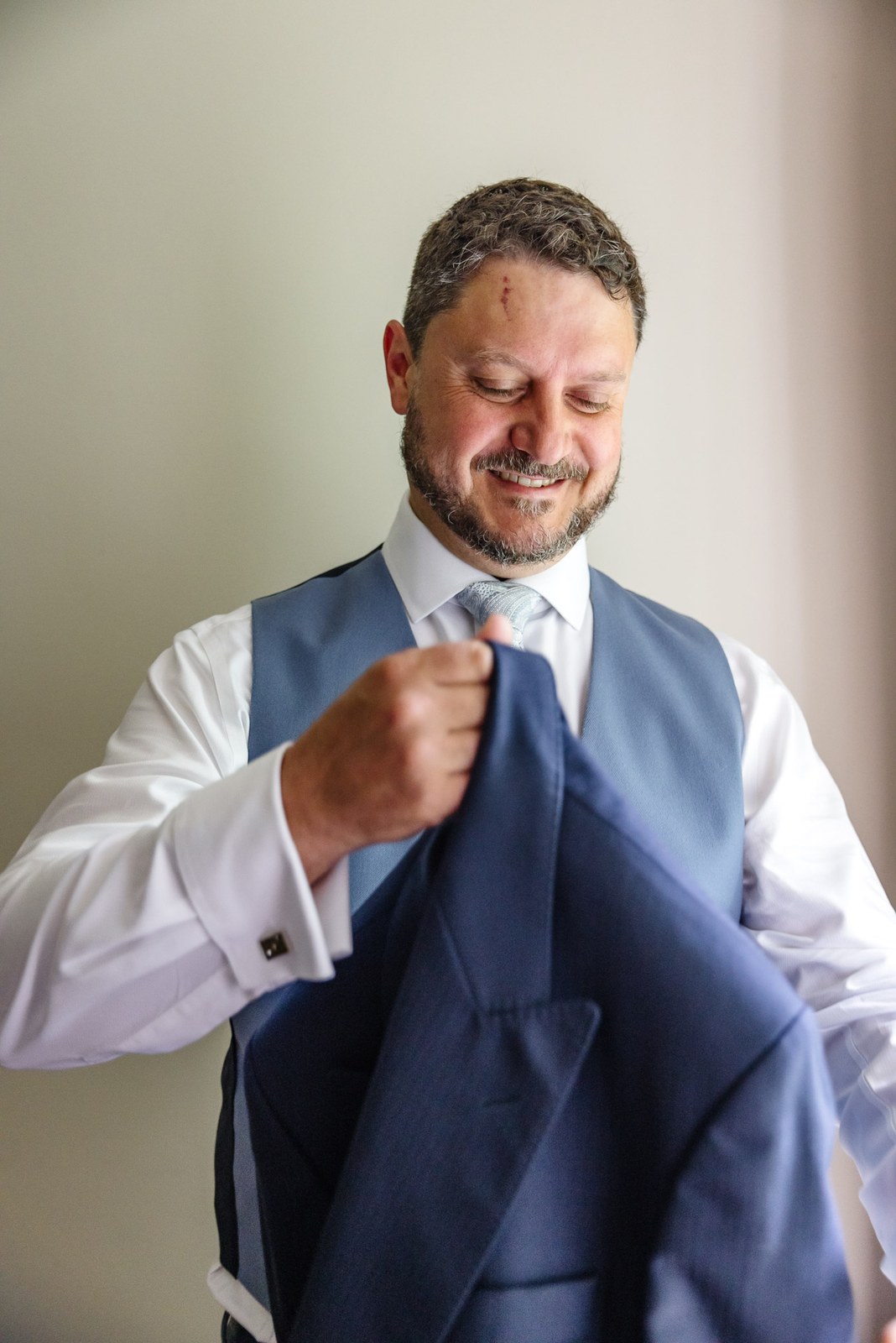 The groom slips on his blue jacket over his waistcoat