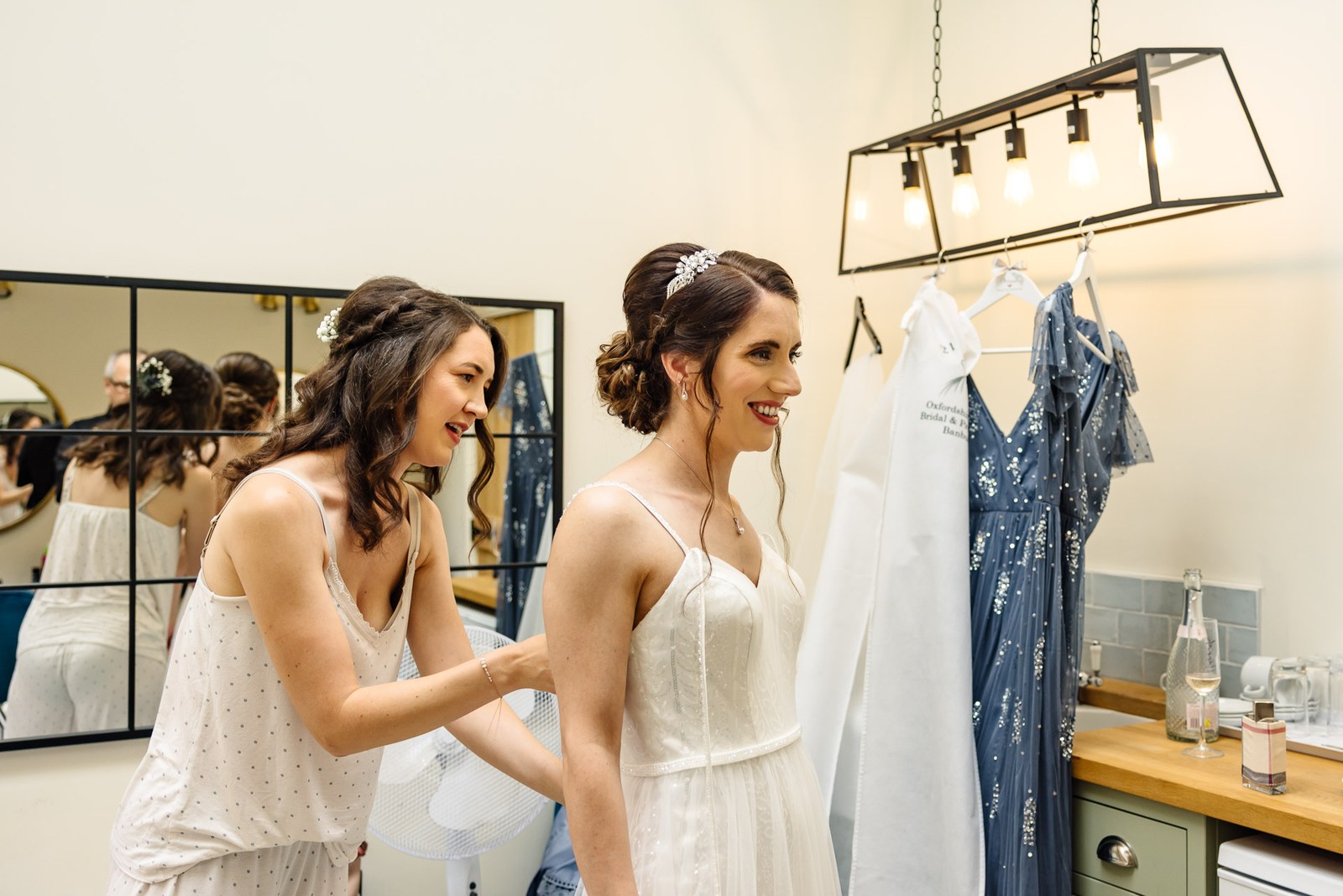 A bridesmaid helps the bride into her gown beside the hanging dresses