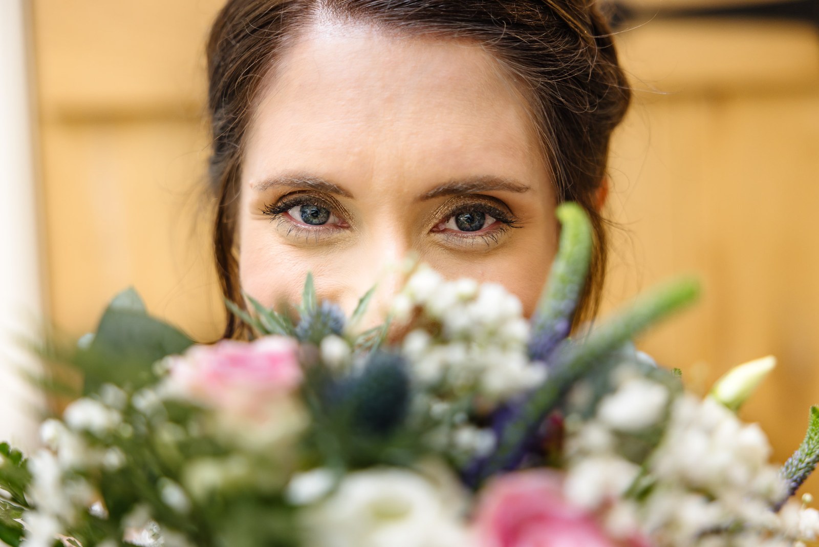 Extreme close-up of the bride's eyes above her bouquet of pastel blooms