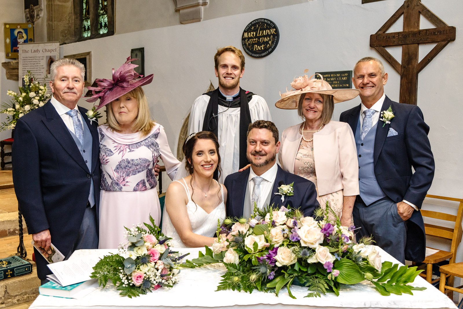 The couple with their parents and the vicar behind the signing table