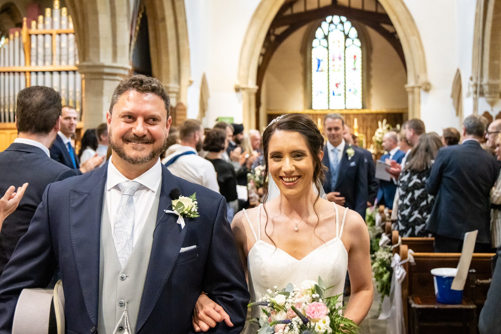The newlyweds walk back down the aisle past the organ, both beaming