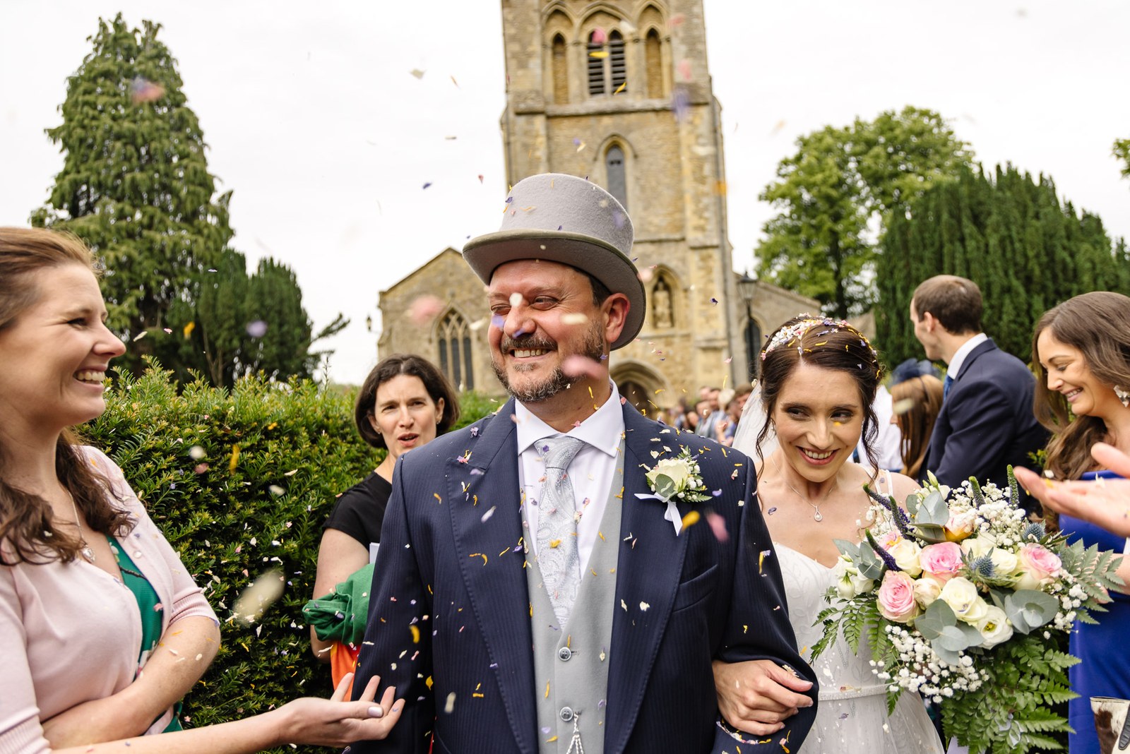 Confetti showers the bride and the top-hatted groom outside the church