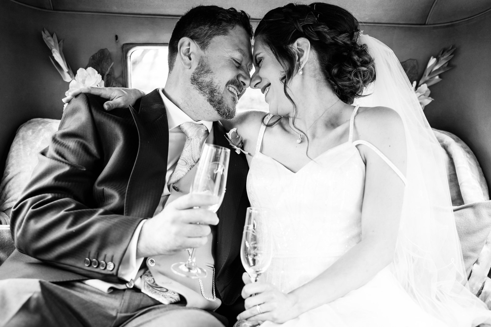 Black-and-white shot of the couple sharing champagne in the back of the car