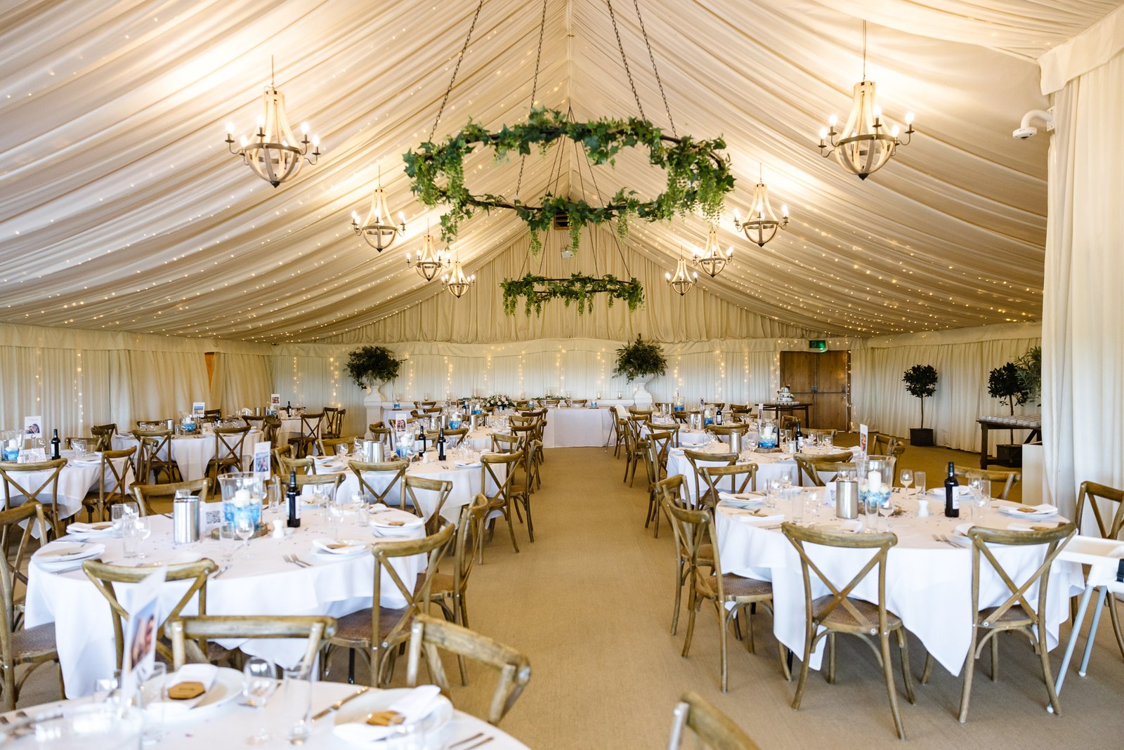 The draped marquee at Crockwell Farm set with round tables beneath foliage-hung chandeliers